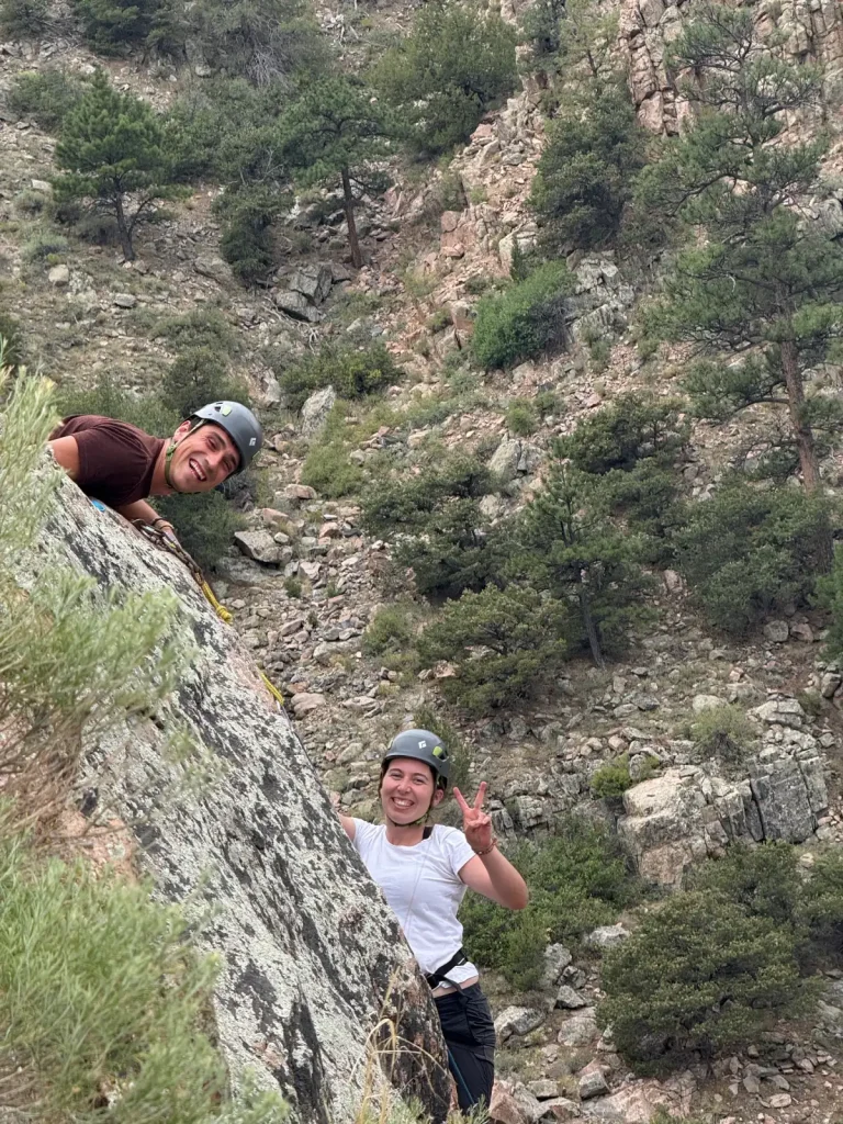 Two rock climbers rappelling down cliff face with safety helmets in desert canyon